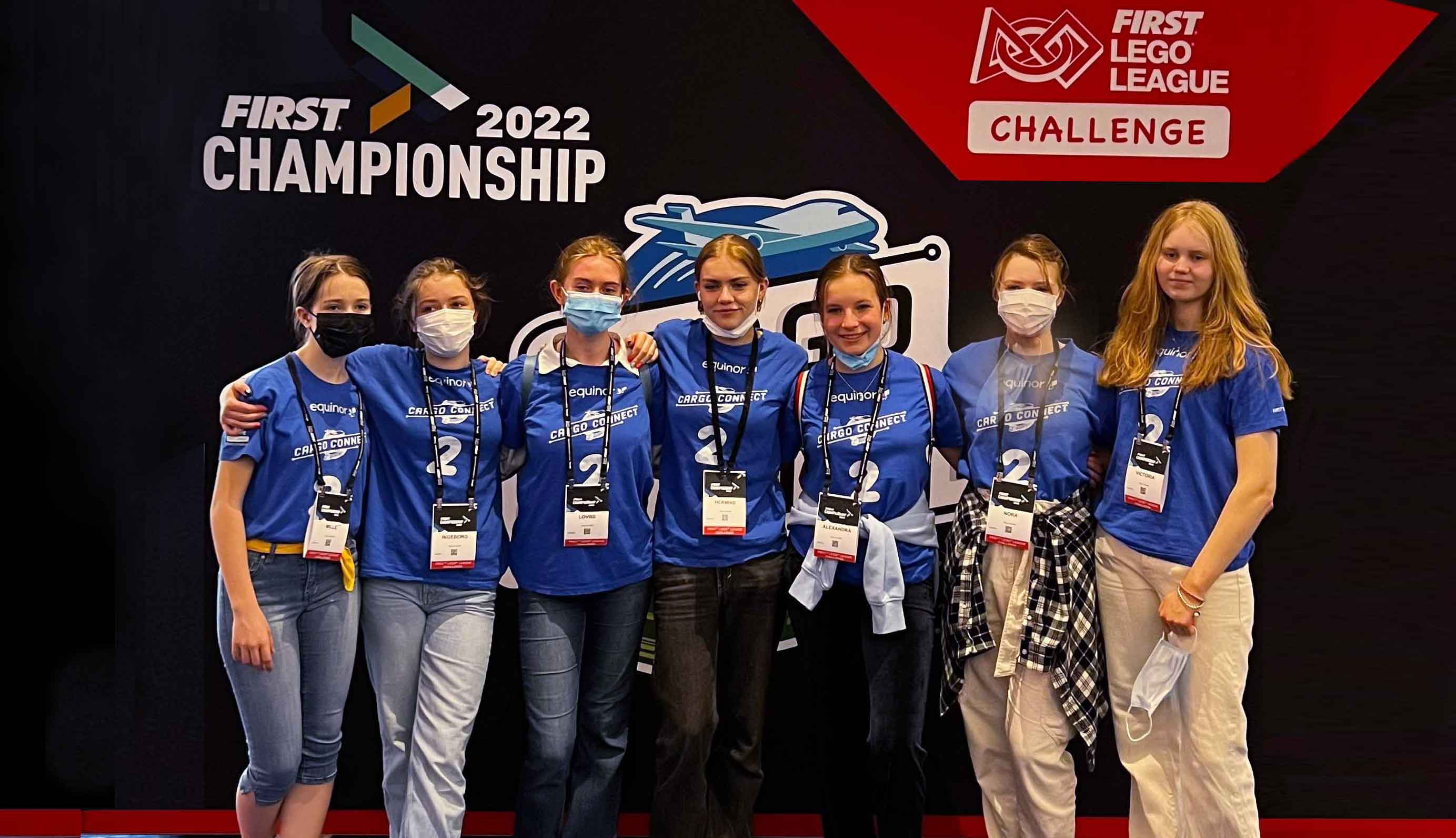 Girls participating in a tech challenge in Texas, smiling in front of a sponsored banner 